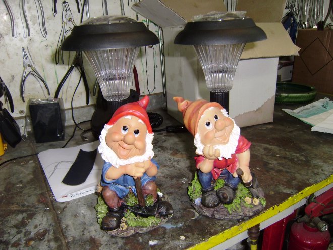 Twee tuinkabouters met lampen met zonnepanelen staan op een werkbank bij White Sails. Wat zijn we ermee van plan? Dat onthullen we morgen