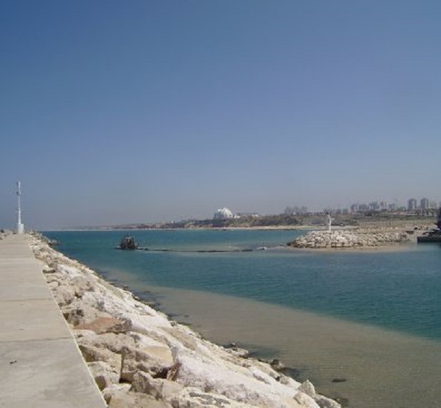 Een baggermolentje poogt ijverig de steeds dichtslibbende haveningang open te houden. Op de achtergrond de koepel van het Holiday Inn hotel